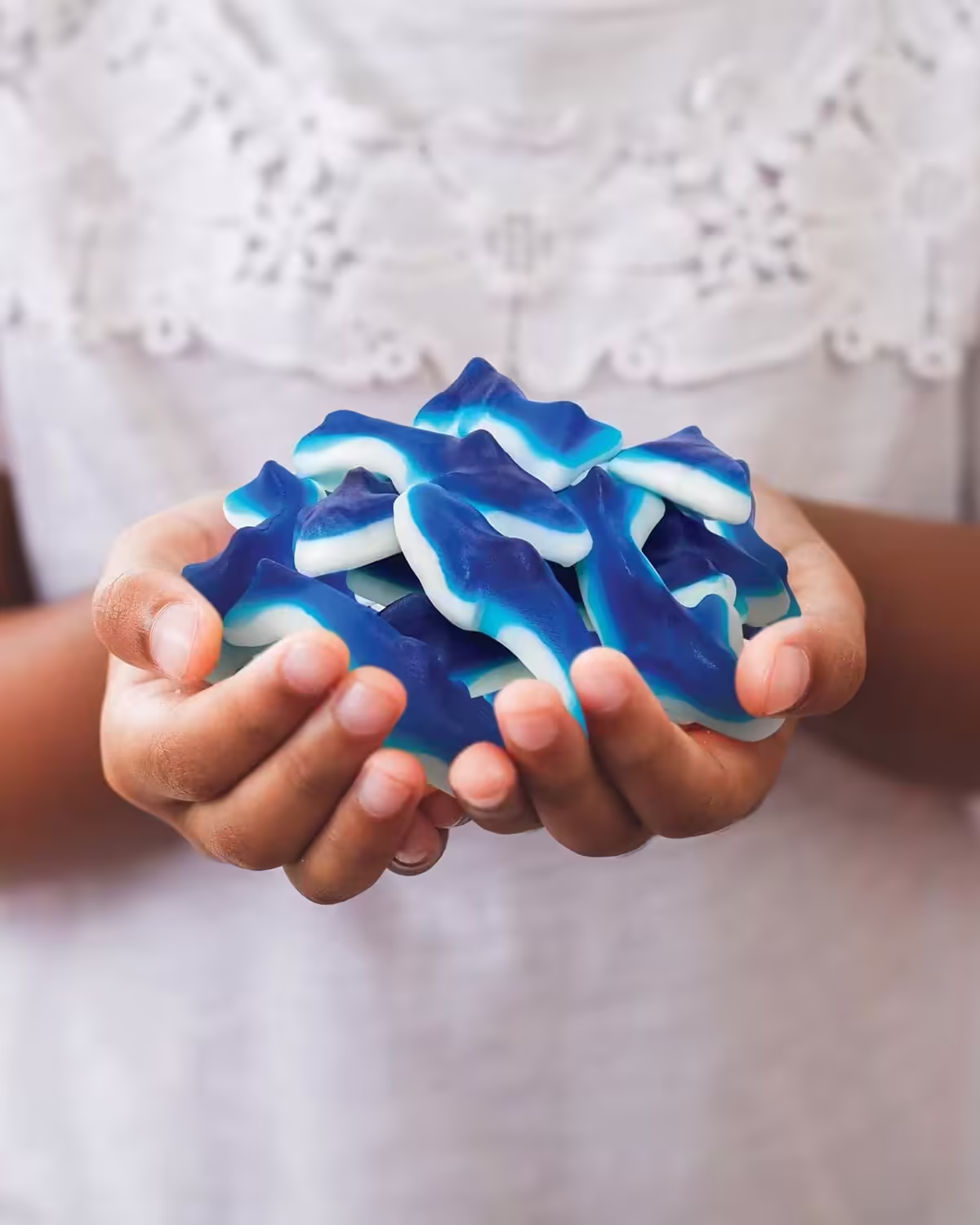 Close-up of a person holding a handful of Blue Sharks Gummy Candy, highlighting the bold blue hue and shark shapes